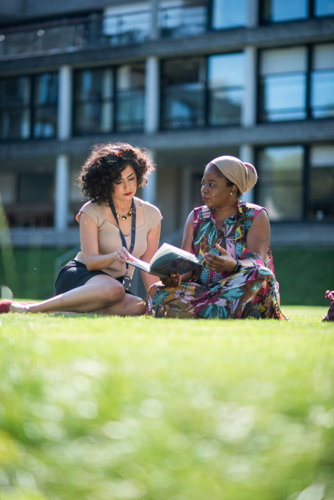 Two students discussing a book on the Harbour lawn